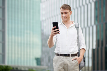 Portrait of confused man reading text message from taxi driver on smartphone