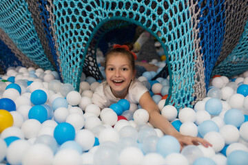 Happy laughing girl playing with toys, colorful balls on the playground, in a dry pool. Little cute...