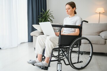 woman in a wheelchair works on the laptop PC in the home office with an assistance dog as a companion