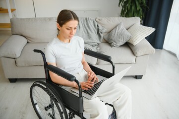 woman in a wheelchair works on the laptop PC in the home office with an assistance dog as a...