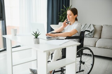 Female freelance programmer sitting in wheelchair and using computers while coding web game at home.