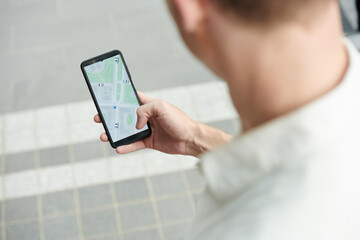 Fototapeta Young man tracking taxi car via application on smartphone, view over shoulder obraz