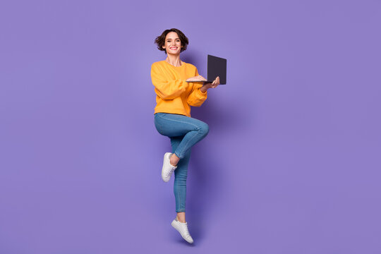 Full length body size view of attractive cheerful girl jumping using netbook isolated over violet lilac color background