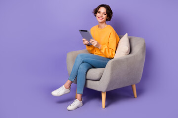Portrait of attractive cheerful girl sitting using gadget reading e book isolated over violet lilac...