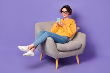 Portrait of attractive cheerful girl sitting using device communicating post video isolated over violet lilac color background