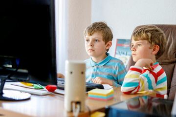 Two little kids boys playing computer games on desktop pc. Modern addict activity for children. Siblings and friends gaming at home.