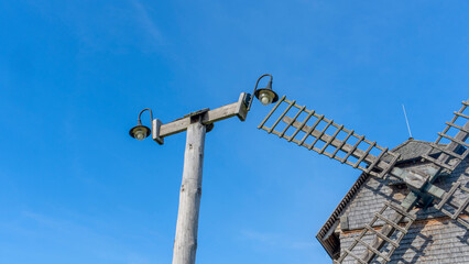Fototapeta na wymiar Vintage wooden windmill with cycling track on blue sky background. Historical farm house windmill.