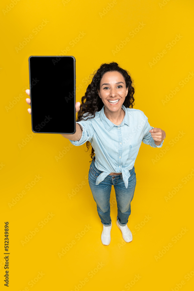 Poster young woman pointing at tablet with empty screen, offering mockup for website or application over ye