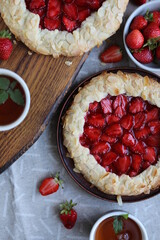 Delicious summer galette with pieces of juicy strawberries. Flat lay with open pies and cups of tea. Summer lunch with berry pastries.