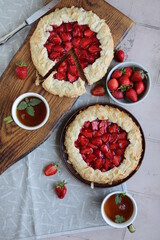 Delicious summer galette with pieces of juicy strawberries. Flat lay with open pies and cups of tea. Summer lunch with berry pastries.