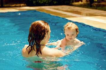 Family happiness. Summer outdoor fun in the pool in the villa. A woman teaches a baby to float on the water and swim. Happy child is having fun. Mom and daughter in the pool
