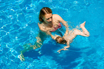 Summer outdoor fun in the pool in the villa. Happy child is having fun. Family happiness. Mom and daughter in the pool. A woman teaches a baby to float on the water and swim