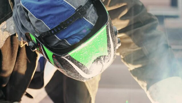 View of welder near pipe at work. Video 4k resolution. Welder in protective mask welds pipe and sparks fly. Industrial construction. Real workflow.