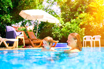 A woman teaches a baby to float on the water and swim. Family happiness. Mom and daughter in the pool. Happy child is having fun. Summer outdoor fun in the pool in the villa