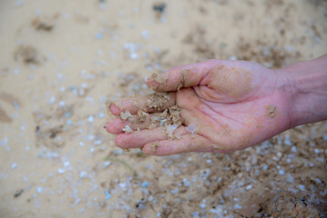 Close up hand grips soil and sand contaminated with micro plastic.
