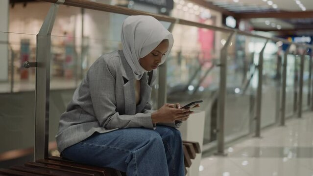 Muslim black woman chats on phone in shopping center hall