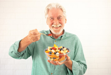 Portrait of smiling senior white-haired man ready to eat a salad of fresh summer fruits. Breakfast...