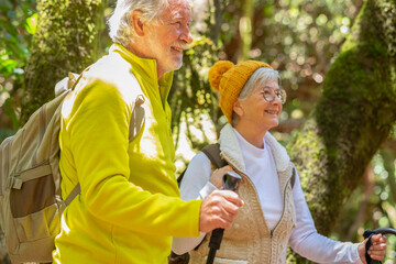 Happy caucasian senior couple with backpack and walking sticks hike in the forest enjoying healthy...