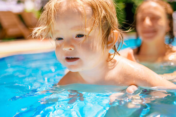 Fototapeta na wymiar The child has fun outdoors in the pool in the villa. Family happiness. Little beautiful girl is splashing in the pool. The baby is learning to swim
