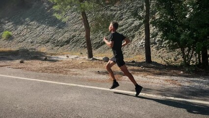 Man running fast on asphalt road in mountains. Male athlete jogging outdoors