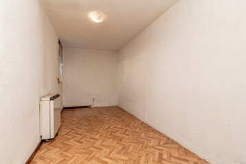 Empty room with herringbone oak parquet flooring and wood carpentry and heat accumulator on the wall