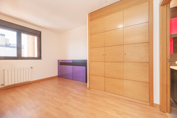 Empty living room with wooden floor, white painted walls, brown aluminum window and built-in wardrobe with oak wood doors
