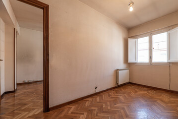 Empty room with bright oak parquet floor, white painted walls and reddish woodwork on white wooden doors and windows with shutters