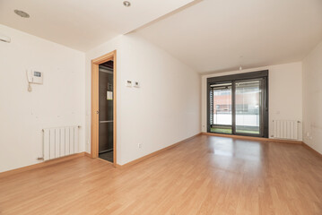 Empty living room with aluminum radiators, exit to a terrace with black aluminum sliding doors and oak parquet floors