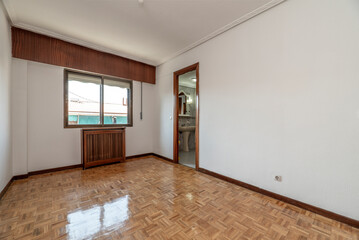 Empty room with wooden radiator cover, bronze-colored aluminum window, wooden carpentry and shiny oak parquet floors