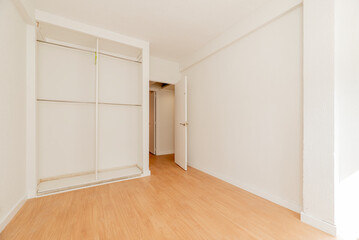 Empty room with oak parquet floor, white painted walls, access to another room and built-in wardrobe with bars