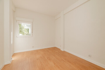 Empty room with oak parquet floor, white painted walls and aluminum windows overlooking a park