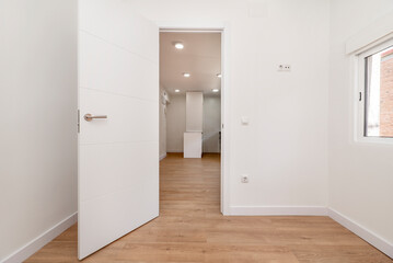 Empty room with oak parquet floor, white painted walls, access to another room and white aluminum windows