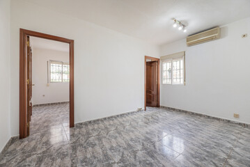 Empty room with plain white painted walls, access doors to two rooms and grayish ceramic stoneware floors