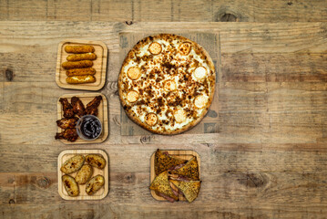 Set of fast food dishes and pizza with goat cheese on wooden table
