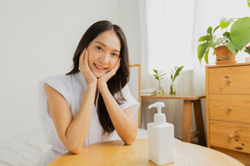 Portrait of beautiful Asian woman with skin lotion cream bottle on table to apply moisturizing on her hand, treatment and body care concept
