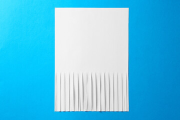 Half shredded sheet of paper on light blue background, top view