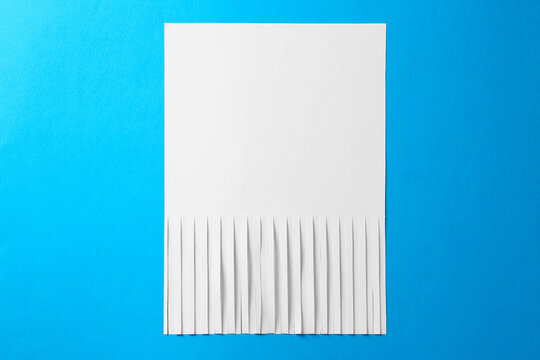 Half shredded sheet of paper on light blue background, top view