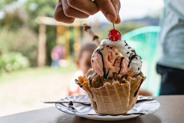 Horizontal image of an unknown person's hand taking the cherry of a delicious ice cream on a table. 