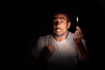Frightened man looking at the camera with a match in the dark. Blackout concept. Selective focus.