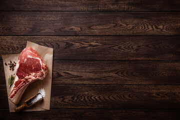 Raw tomahawk or cowboy beef steak on piece of craft paper over wooden background. Top view with...