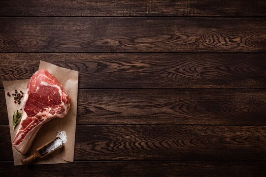 Raw tomahawk or cowboy beef steak on piece of craft paper over wooden background. Top view with copy space
