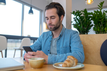 Man reading message on smartphone sitting at table