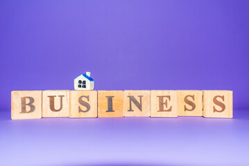 BUSINESS word written on wood blocks,miniature toy house and number cubes put on purple ,veri peri background.Copy space.