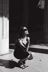 A beautiful girl with a hairstyle in a black dress on the street with a cigarette in her hands smokes, black and white photo.
