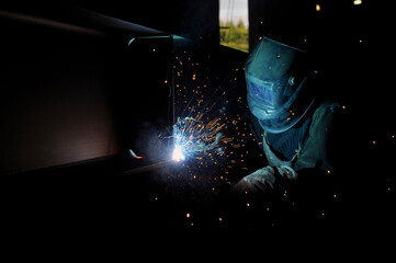 A welder in protective overalls and a welding mask welds metal structures by welding on a...