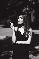 A beautiful girl with a hairstyle in a black dress on the street with a cigarette in her hands...