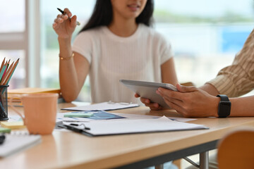 Cropped view of good looking Asian businesswoman having a conversation in an office with a male coworker, working on a tablet and paperwork together, for business and technology concept.