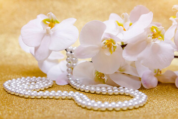 Fototapeta na wymiar white Orchid and pearl necklace on a shiny gold background