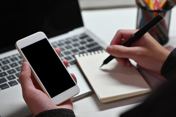 Close up of a man sitting in the office working on a laptop, using a smart phone and taking a note. For business, technology and home concept.