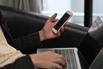 Close up of a man sitting on a sofa and working on a laptop and a smart phone. For business, technology and home concept.